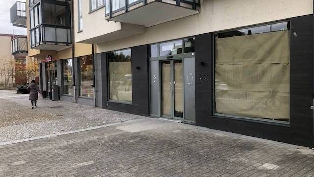 En gatuvy av en modern byggnad med stora fönster täckta av brunt papper; en person går på trottoaren i närheten.
