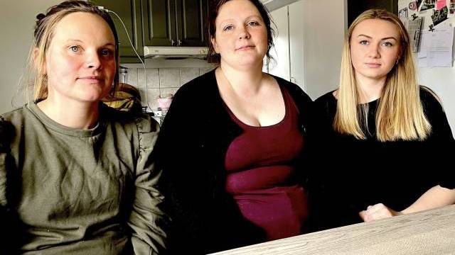 Tre kvinnor som sitter vid ett köksbord och tittar på kameran. köket har gröna skåp och ett kylskåp i bakgrunden.