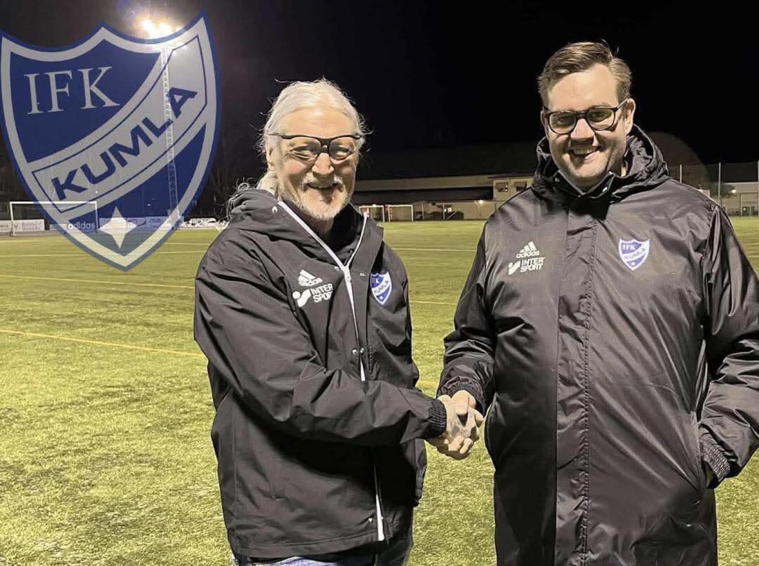 Två män i svarta jackor skakar hand på en fotbollsplan på natten, med en IFK Kumla-logga i bakgrunden.