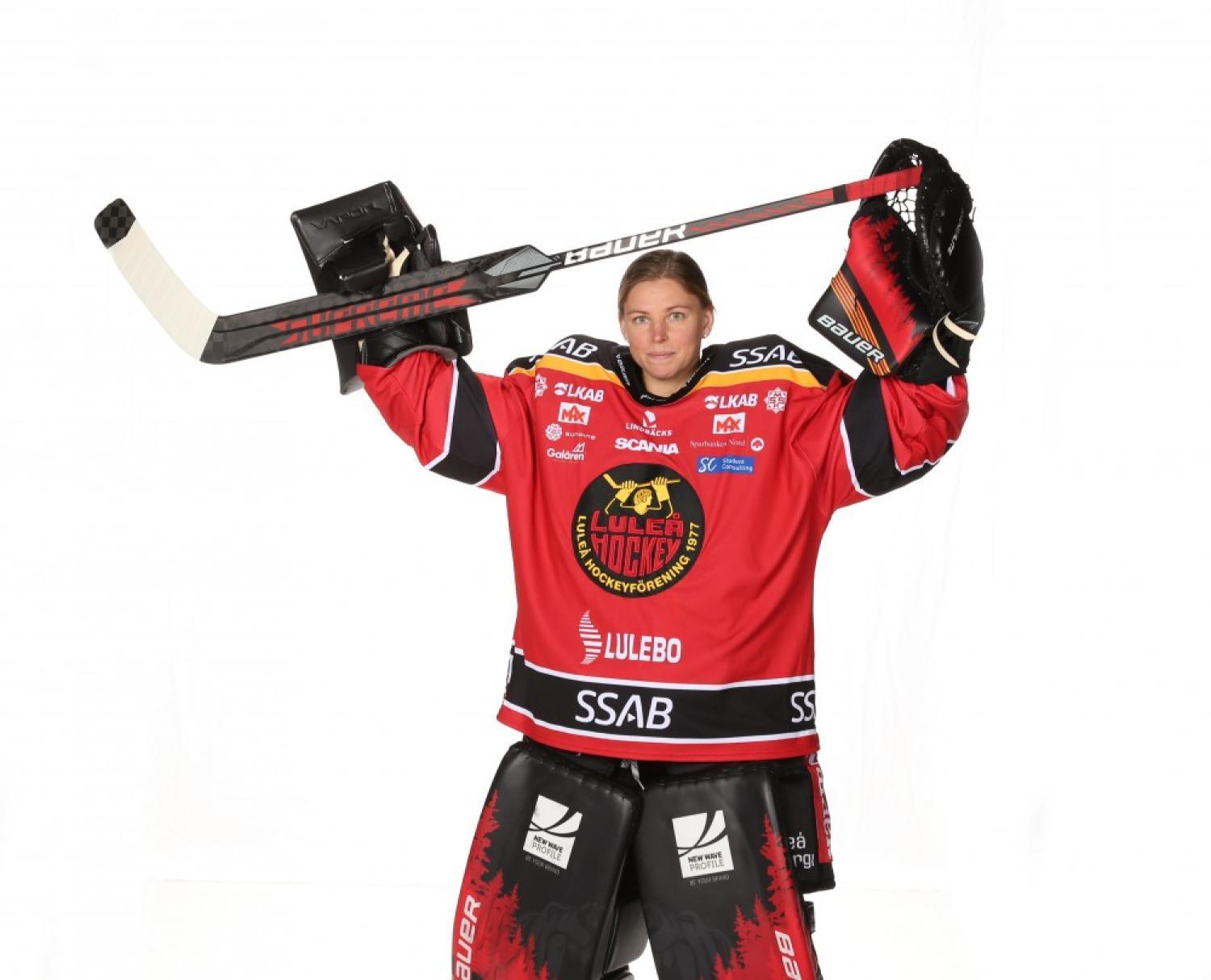 Hockeyspelare i röd och svart uniform håller en hockeyklubba ovanför huvudet. Uniformen har olika logotyper inklusive