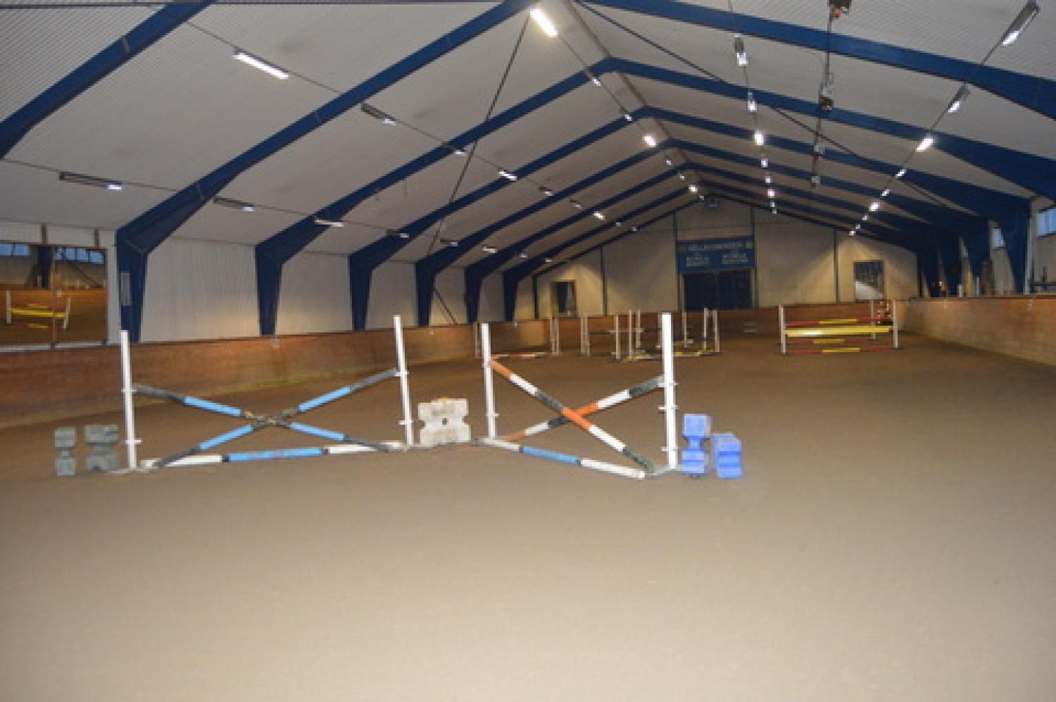 Ridarena inomhus med olika färgade hopp arrangerade på smutsgolvet och en skylt med texten