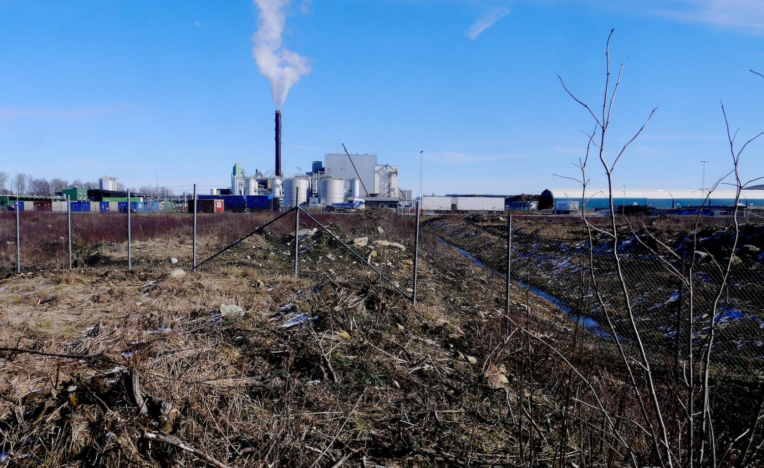 Industrianläggning med skorsten bortom ett inhägnat fält.