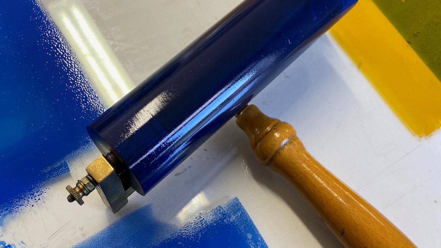 En blå bläckrulle med trähandtag ligger på en vit yta med blå och gula bläckfläckar.