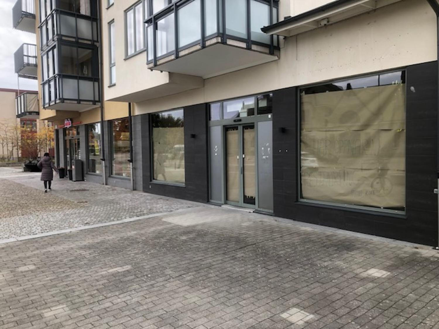 En gatuvy av en modern byggnad med stora fönster täckta av brunt papper; en person går på trottoaren i närheten.