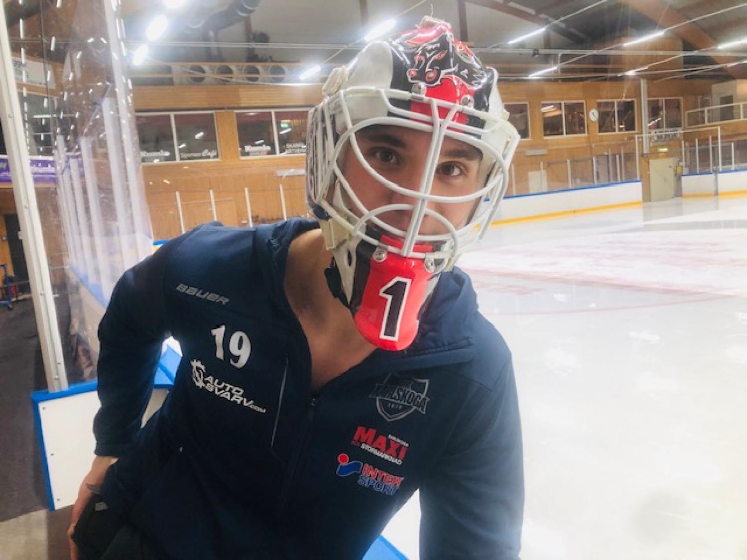 En hockeymålvakt iförd mask och tröja står på en inomhusisbana och tittar mot kameran.