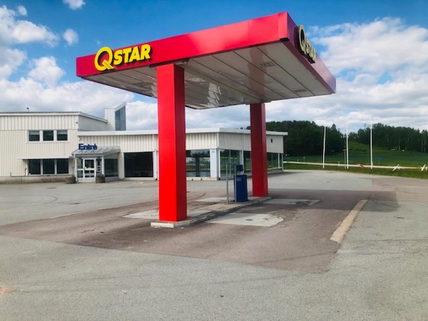 En Qstar-mack med rött skärmtak står obevakad framför en vit byggnad under en delvis molnig himmel. Området ser tomt och lugnt ut.