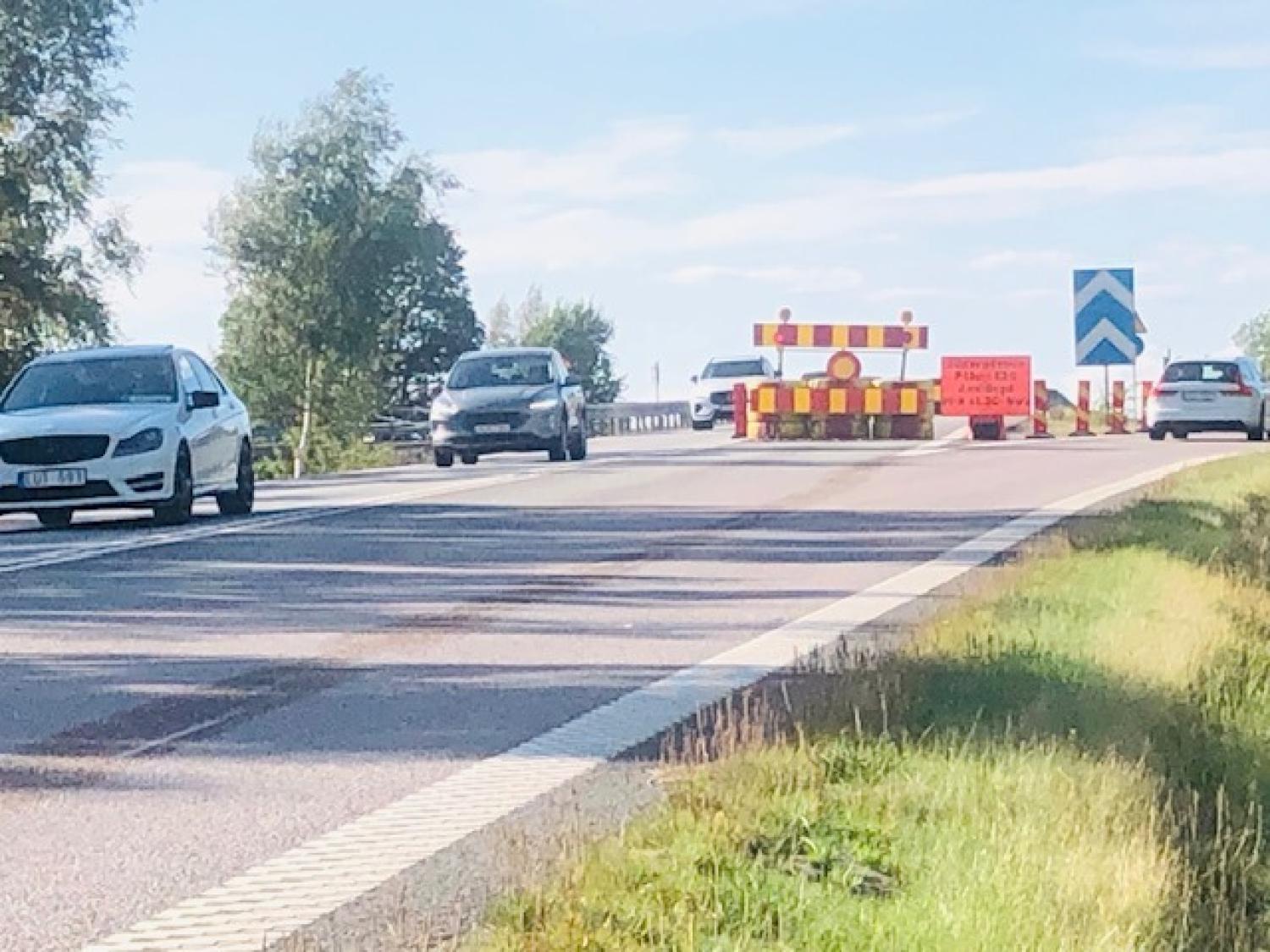 Bilar närmar sig en vägspärr med skyltar och avspärrningar som anger att ett körfält är avstängt en solig dag.