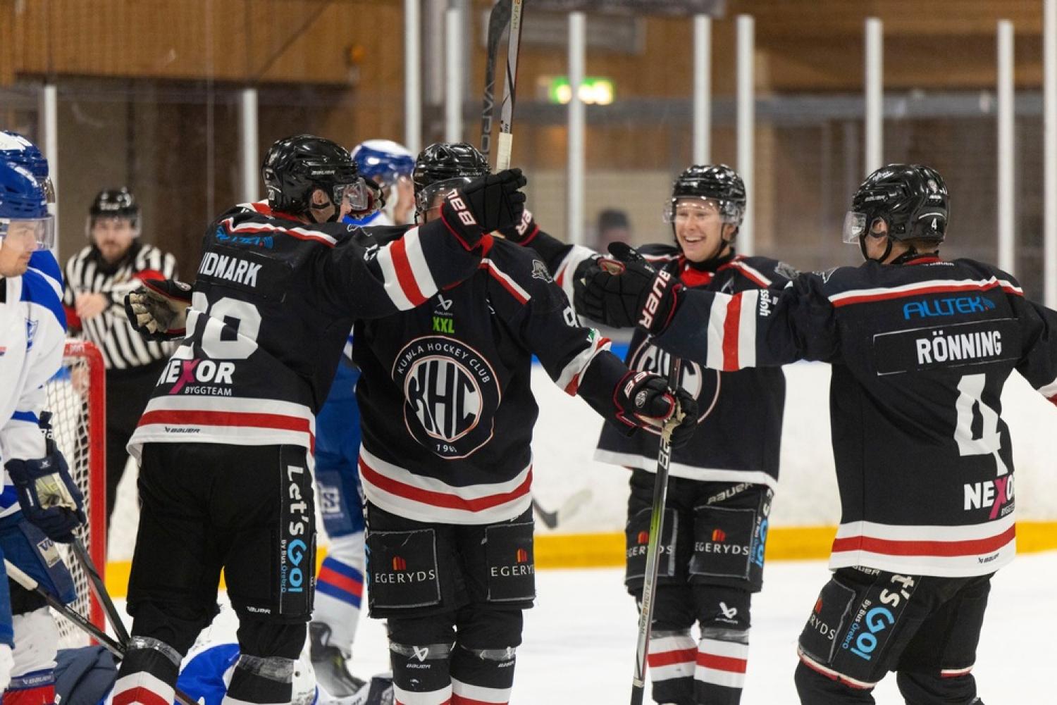 Hockeyspelare i svarta tröjor firar ett mål på ishallen och höjer sina pinnar i luften. En spelare i blå tröja och en domare syns i bakgrunden.