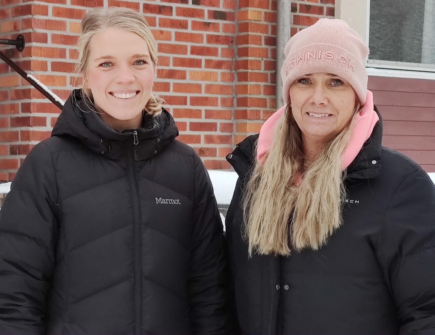 Två kvinnor i svarta jackor som står framför en byggnad.