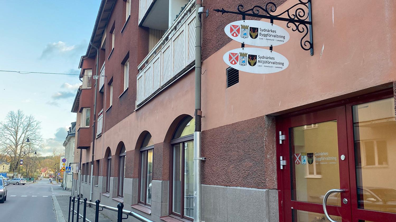 På en lugn gata ligger en röd byggnad med välvda fönster och en glasdörr med en skylt för