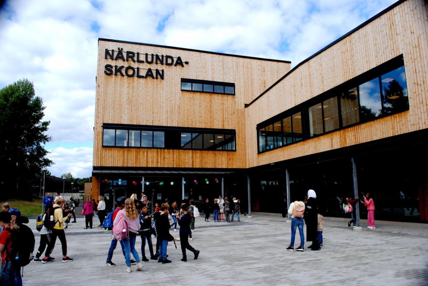 Flera elever samlas utanför en stor modern träbyggnad med skylten