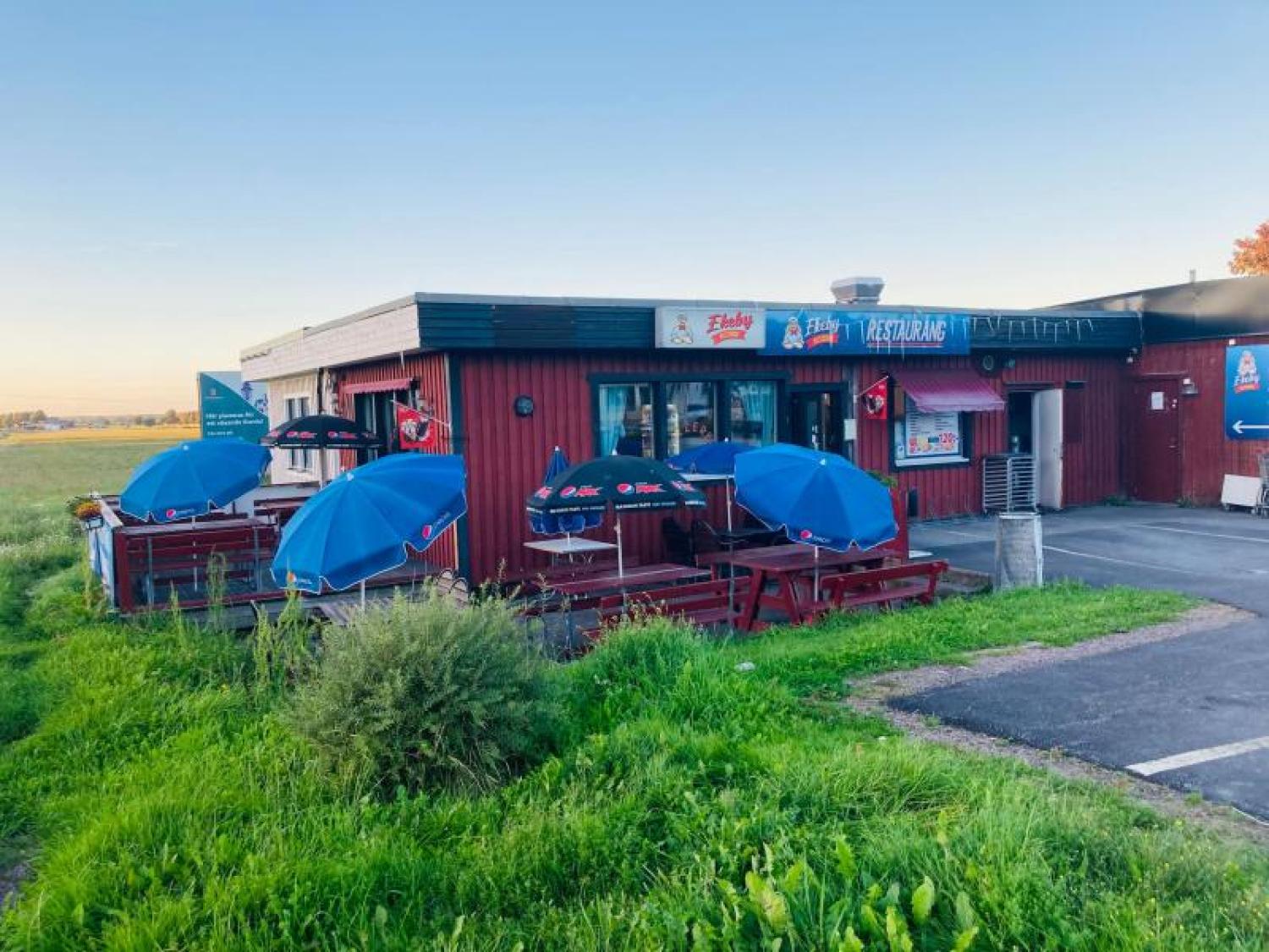 En liten röd restaurang med uteservering, blå parasoller och en skylt med texten