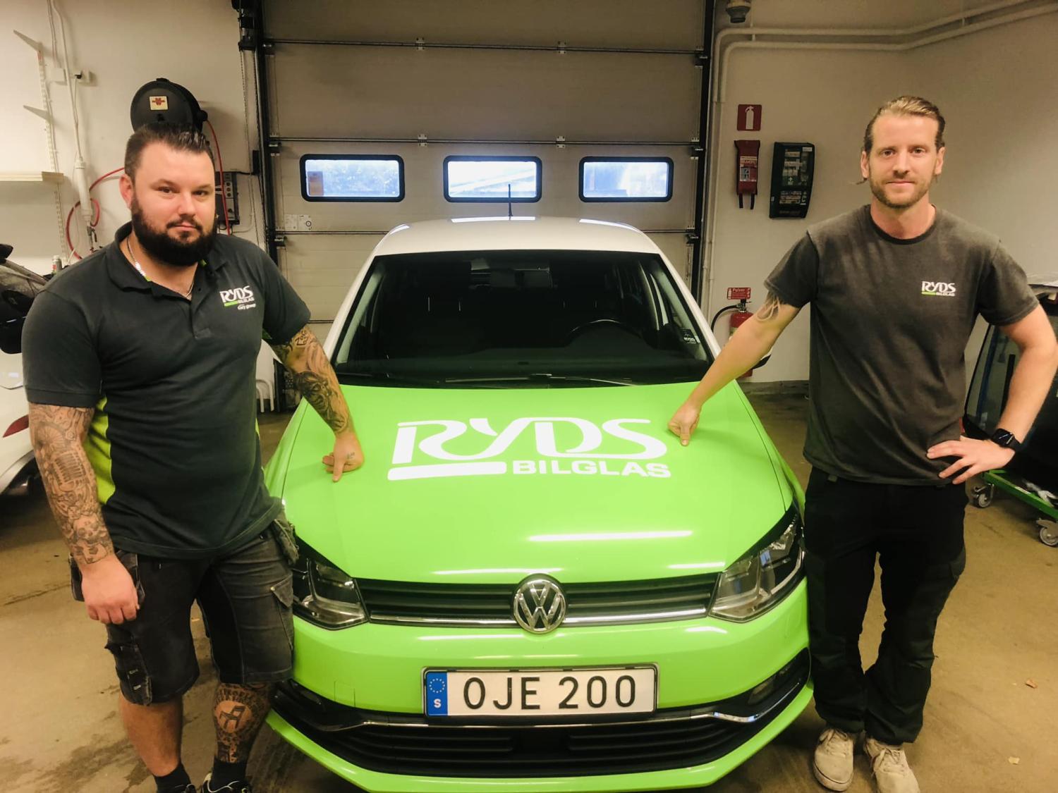Två män som står bredvid en knallgrön Volkswagen med