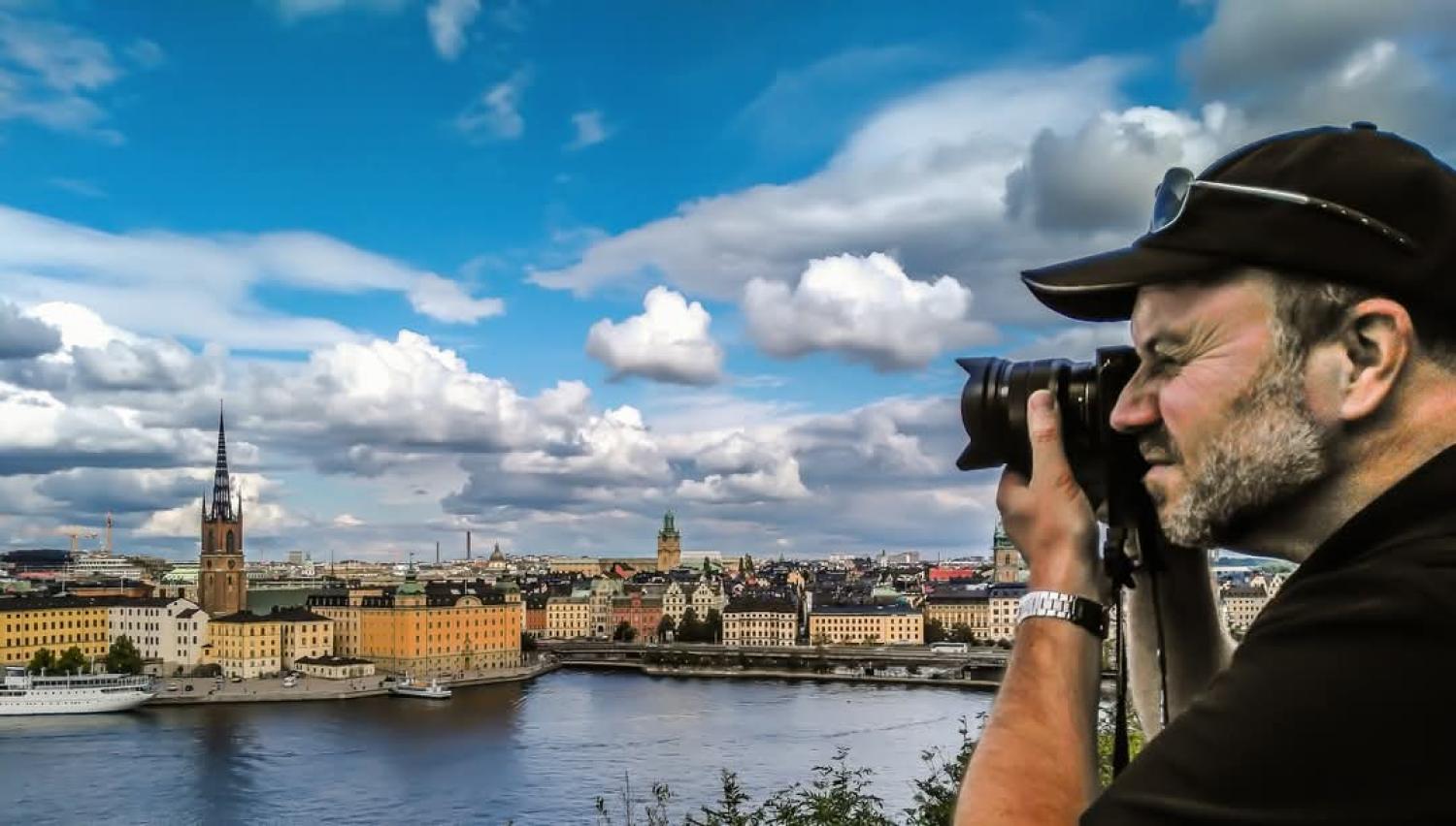 Man fotograferar en stadsbild med vatten och historiska byggnader under en delvis molnig himmel.