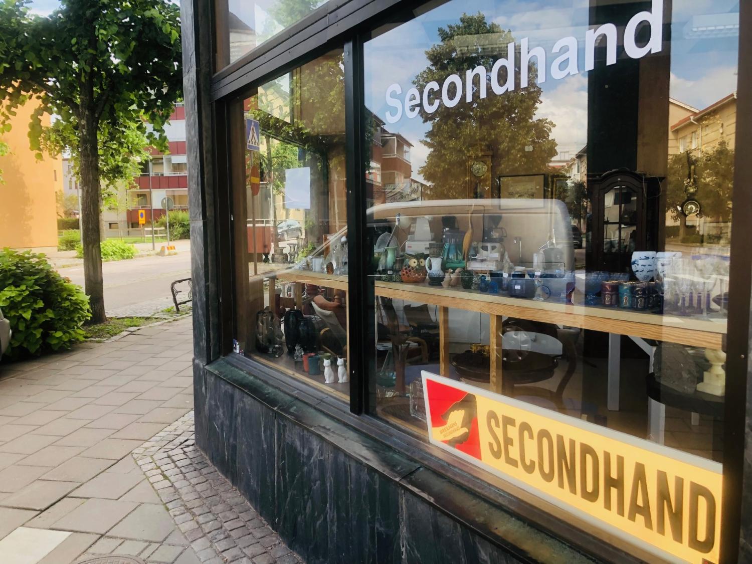 En gatuvy över en secondhandbutik med varor utställda i fönstret och två