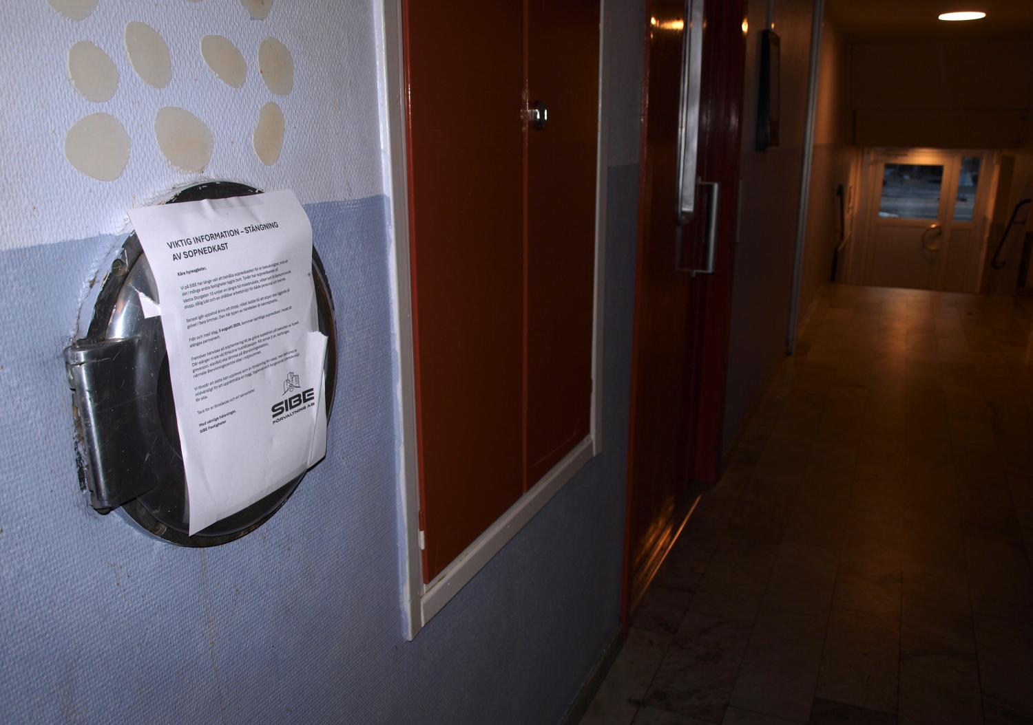 Ett meddelande är fasttejpat på en väggmonterad cirkulär container i en svagt upplyst hall med klinkergolv och dörrar längs väggarna.
