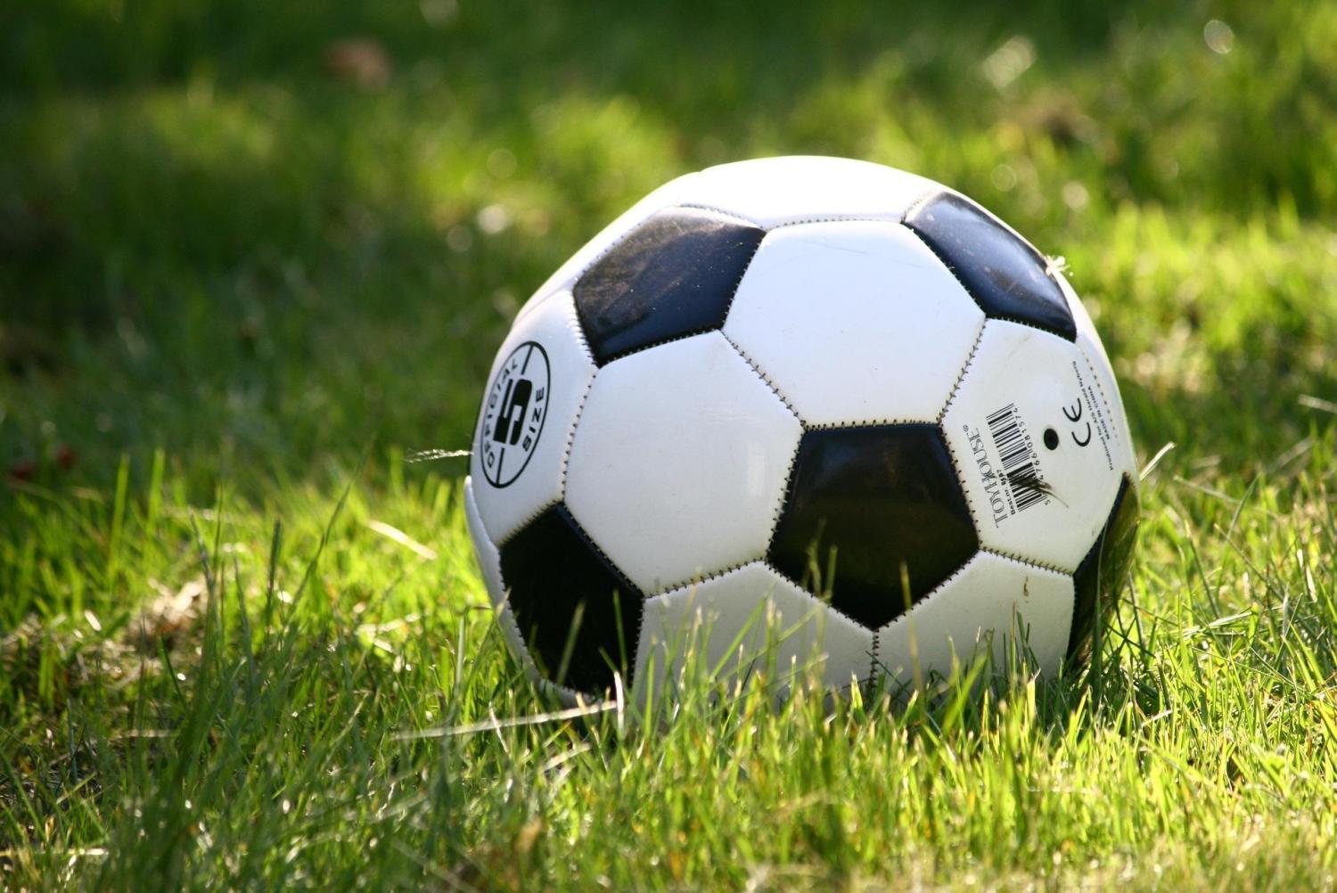 En svartvit fotboll ligger på grönt gräs i solskenet.