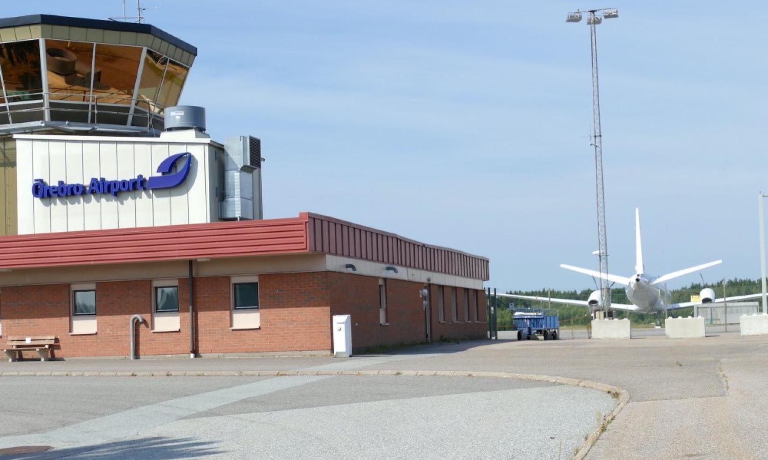 Ett plan står parkerat framför ett flygplatskontrolltorn.