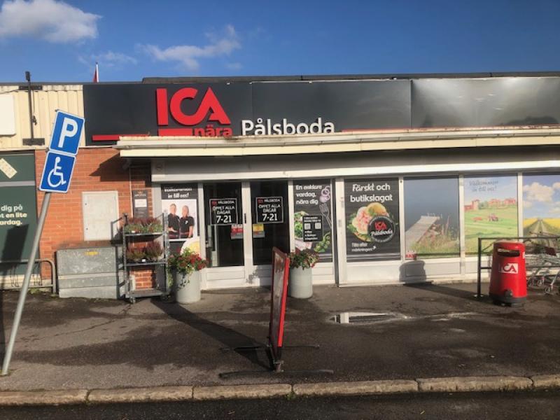 Exteriör av ICA Nära Pålsboda med skyltar, fönster, handikapparkering, blommor och en röd soptunna vid entrén.