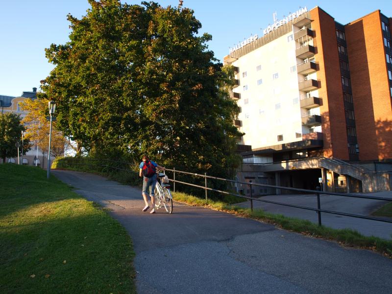 En person cyklar på en asfalterad väg som slingrar sig nära en stor byggnad med texten