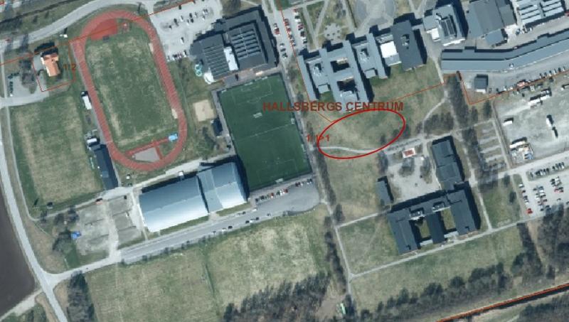 Flygfoto över en idrottsanläggning med fotbollsplan, löparbana, byggnader, parkeringsplatser och ett område märkt