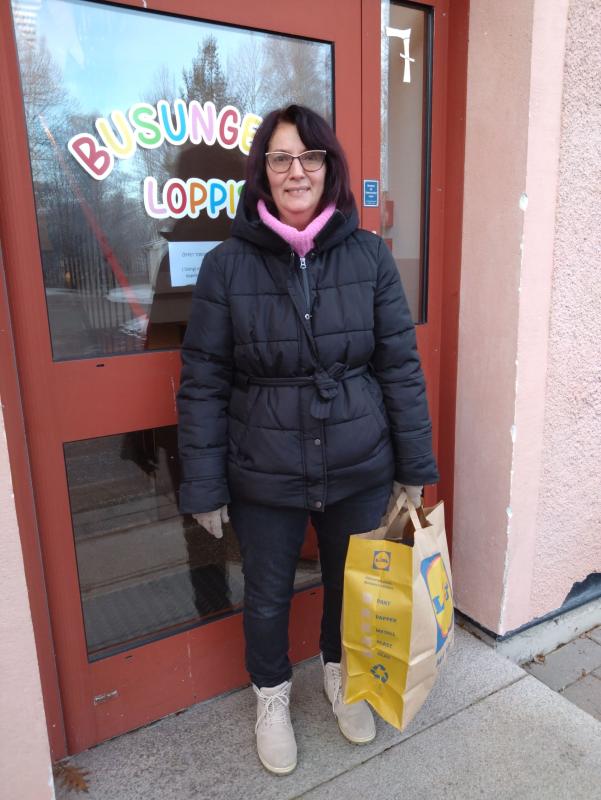 Person i en svart rock som håller en shoppingväska, står framför en röd dörr med färgglad text.