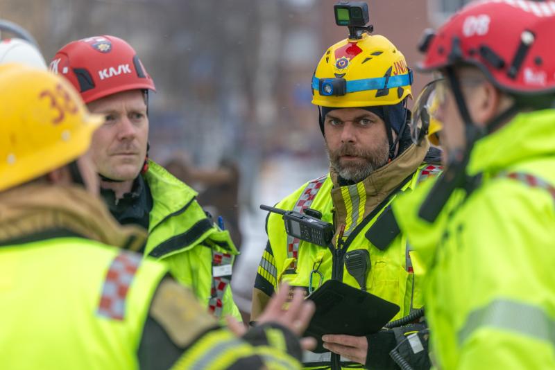 Fyra räddningspersonal i ljusgula jackor och hjälmar står utomhus och samtalar under vad som verkar vara en samordnad insats eller genomgång.
