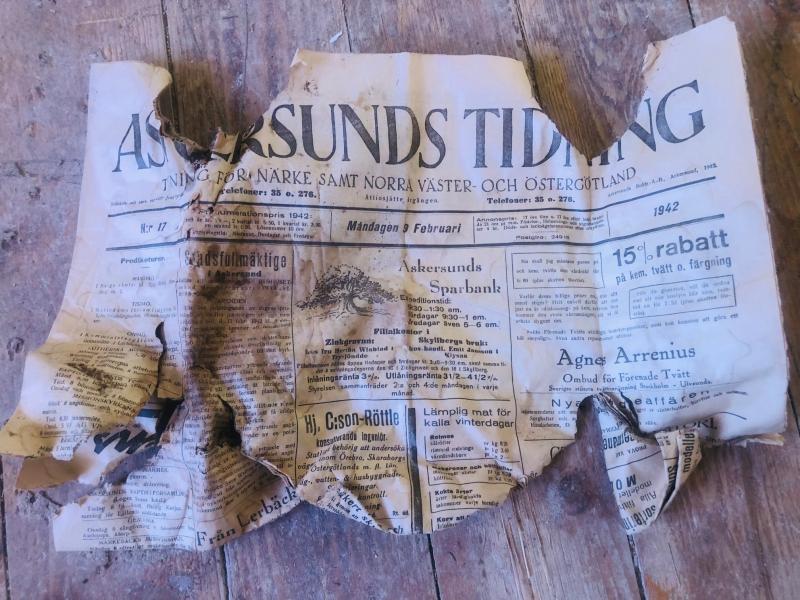 En sönderriven och fläckig sida ur Askersunds Tidning ligger på ett slitet trägolv.