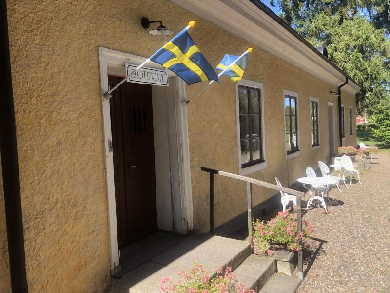 En beige stuckaturbyggnad med två svenska flaggor ovanför dörren märkt 