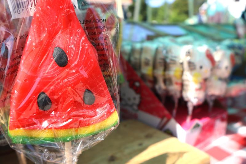 I förgrunden syns en vattenmelonformad klubba inslagen i plast, medan andra färgglada godisar skymtar i den suddiga bakgrunden.