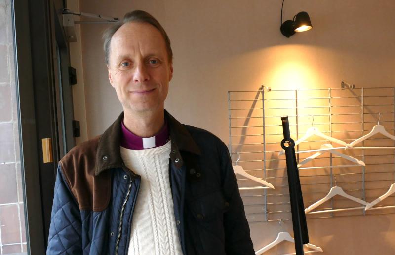 En präst som står framför ett klädställ.