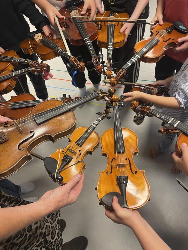 En grupp människor som står i en cirkel håller violiner och violer mot mitten och visar instrumenten ovanifrån.