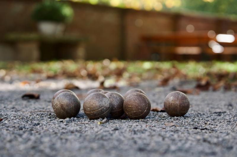 Sex boccebollar ligger på en grusbana med en suddig bakgrund bestående av en vägg, en bänk, grönska och utspridda löv.