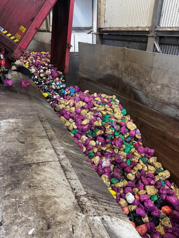 En lastbil lastar av ett stort antal färgglada plastpåsar fyllda med avfall på golvet i en anläggning för hantering av industriavfall.