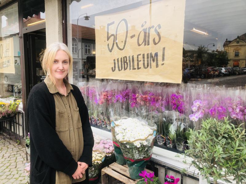 En kvinna står framför en blomsteraffär med skylten 