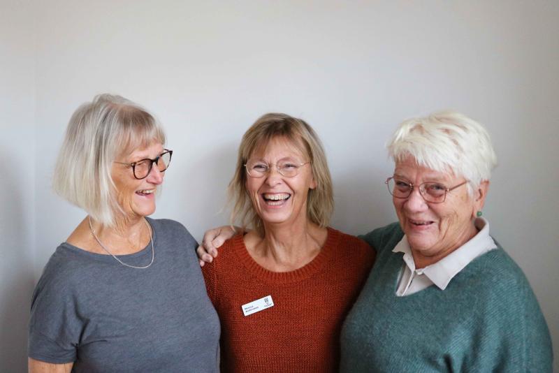 Tre leende kvinnor i olika åldrar, möjligen familjemedlemmar, som står nära varandra mot en neutral bakgrund.