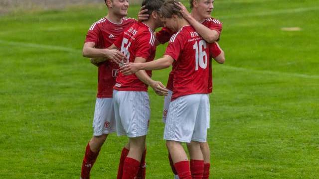 Fyra fotbollsspelare i röda tröjor står på en gräsplan och firar och kramar varandra under en match.