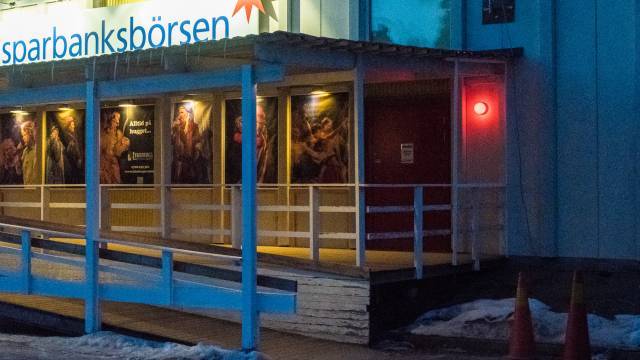 En byggnad med en skylt där det står ”sparbanksbörsen”, en ramp, en röd dörr med en tänd röd lampa och affischer på väggen; snö och orangea trafikkoner syns.