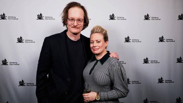 En man och en kvinna poserar tillsammans framför en kuliss från Göteborg Film Festival; kvinnan håller i ett glas vin.