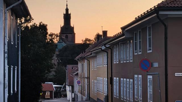 En gata kantad av byggnader vid solnedgången, med ett kyrktorn synligt i bakgrunden och en parkeringsförbudsskylt till höger.