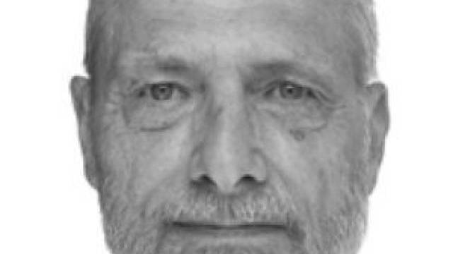 Svartvitt porträtt av en äldre man med kort hår, vältrimmat skägg och neutralt ansiktsuttryck, vänd framåt mot en enfärgad bakgrund.