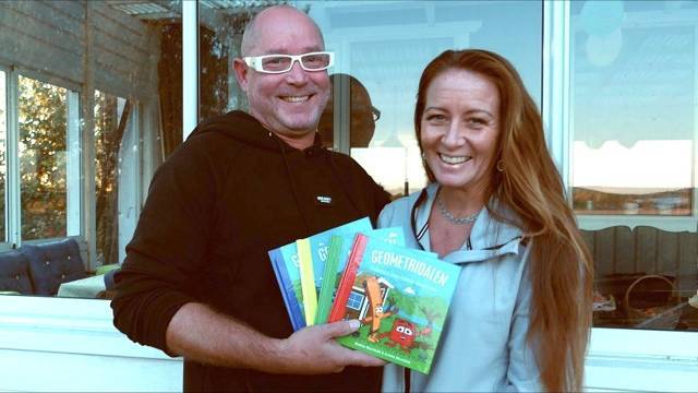 Två vuxna står framför ett fönster och ler medan de håller i en samling färgglada barnböcker.