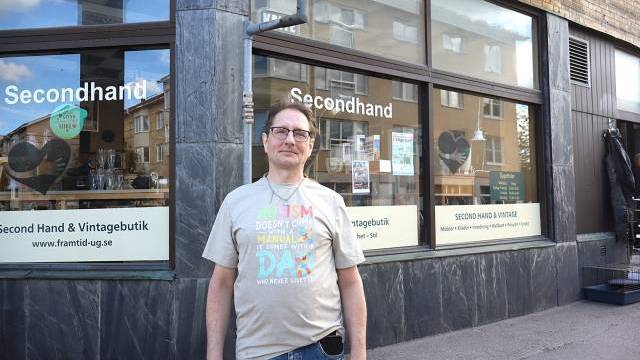En man står utanför en secondhand- och vintagebutik med stora fönster på en gata i stan.