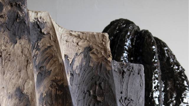 Närbild av två abstrakta keramikskulpturer, den ena med en strukturerad mattbrun yta i förgrunden och en blank svart rundad form i bakgrunden.