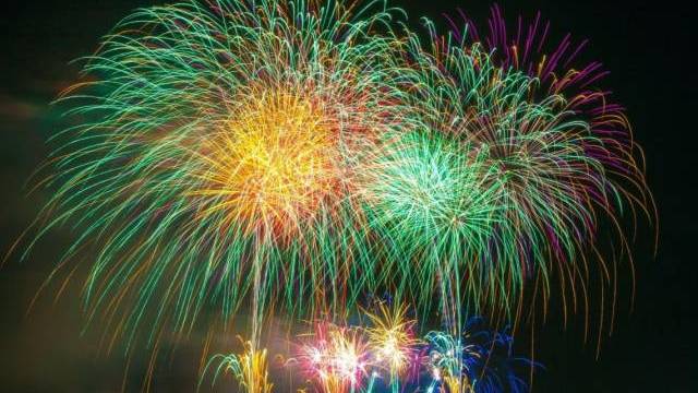 Färgglada fyrverkerier exploderar på natthimlen över en mörk stadsbild, med flera livfulla mönster och ljusstrimmor.