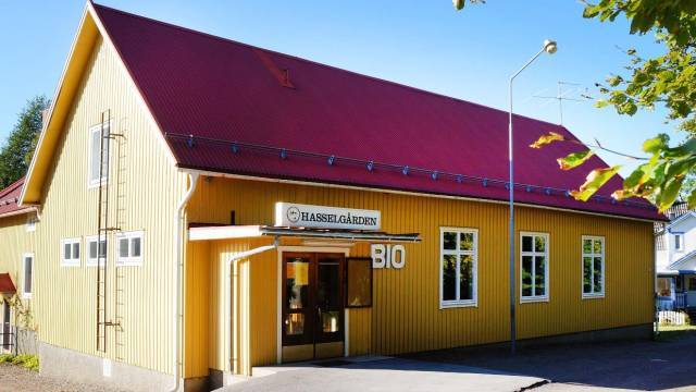 En gul träbyggnad med rött tak, med skylten ”Hasselgården BIO”, under en klarblå himmel.