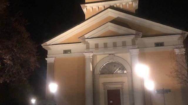 En gul kyrkobyggnad med vita pelare är upplyst på natten, med gatlyktor och nedfallna löv synliga framför.