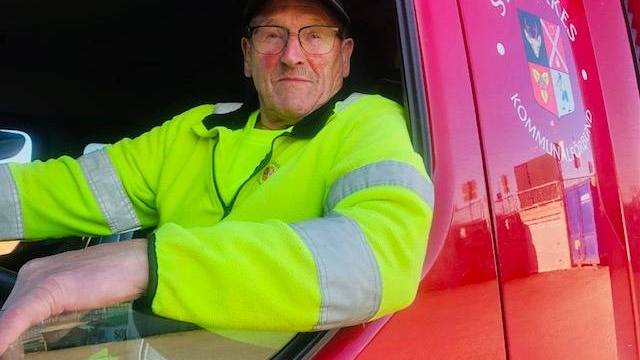 En man i gul varseljacka sitter i förarsätet på ett rött fordon. På dörren syns en logotyp och en text som delvis lyder 