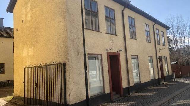 Tvåvåningsbyggnad i gul stuckatur med bruna detaljer och flera fönster, belägen på en kullerstensgata under en klar himmel.