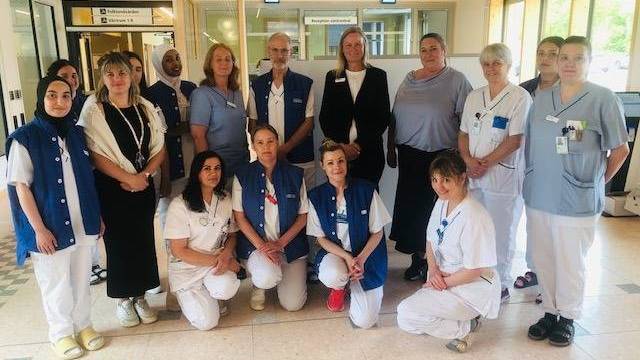 En grupp vårdpersonal i uniform poserar för ett foto inne på en vårdcentral nära en skylt med texten 